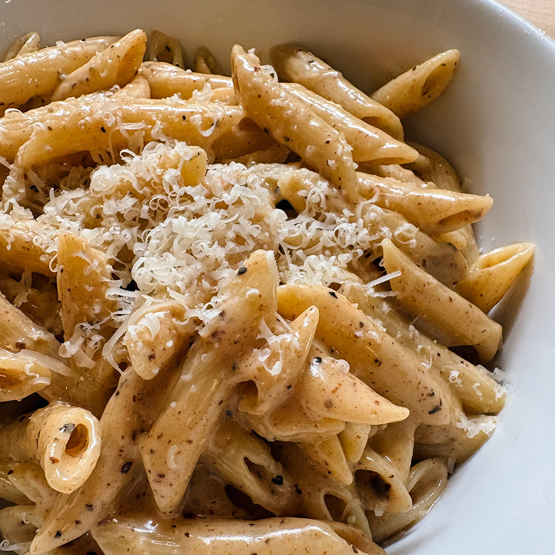 Cacio e Pepe pasta made with Pastacraft pasta sauce starter. Close-up of penne pasta in a creamy cacio e pepe sauce, topped with shredded parmesan cheese and black pepper, served in a white bowl.